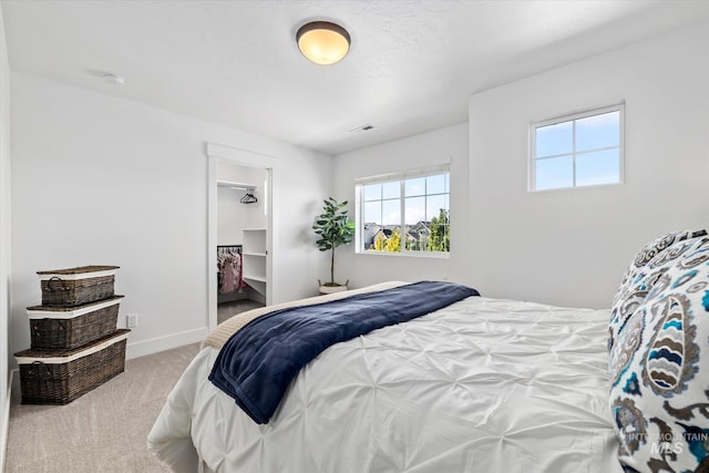 carpeted bedroom featuring visible vents, a walk in closet, and baseboards