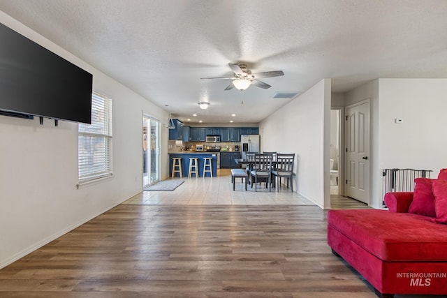 living room with a textured ceiling, ceiling fan, and wood-type flooring