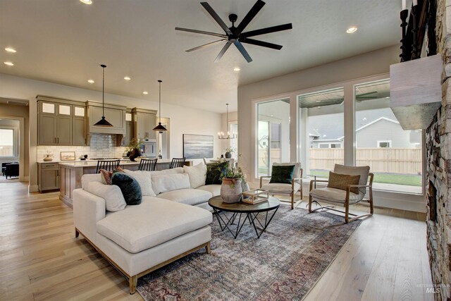 kitchen with light hardwood / wood-style floors, appliances with stainless steel finishes, a kitchen island with sink, decorative backsplash, and pendant lighting