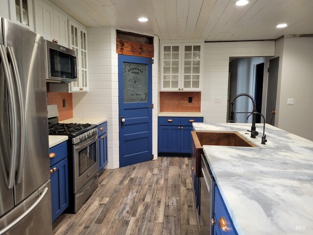 kitchen with white cabinets, blue cabinets, decorative backsplash, appliances with stainless steel finishes, and dark hardwood / wood-style flooring