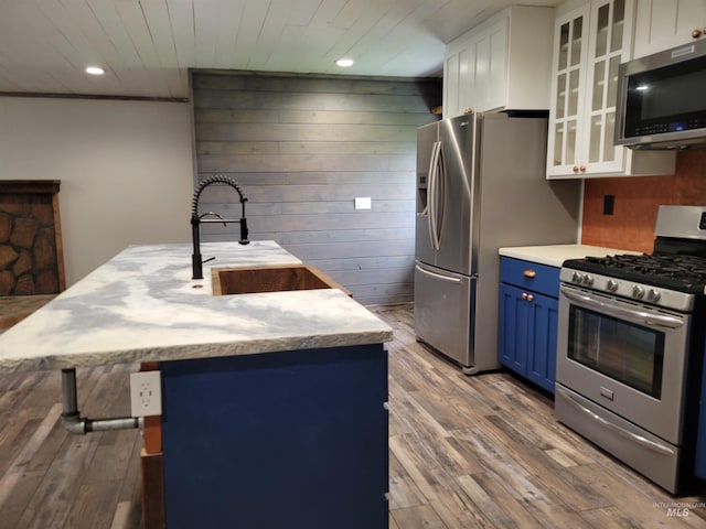 kitchen with sink, blue cabinetry, appliances with stainless steel finishes, white cabinetry, and wood-type flooring