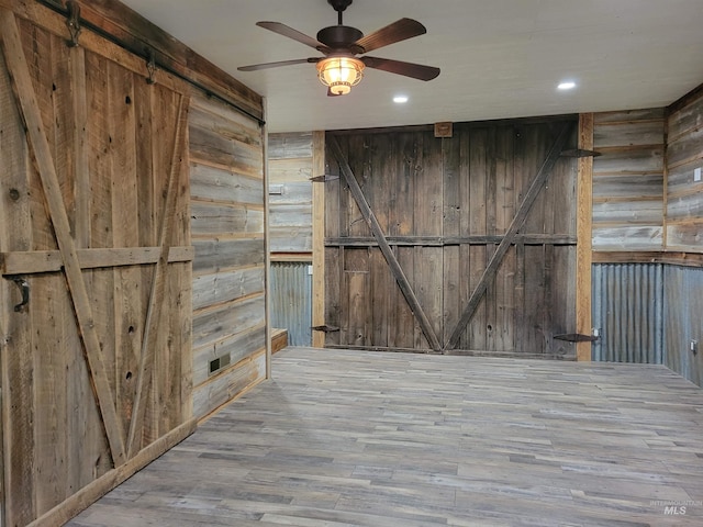 spare room featuring ceiling fan, wood walls, a barn door, and light hardwood / wood-style flooring