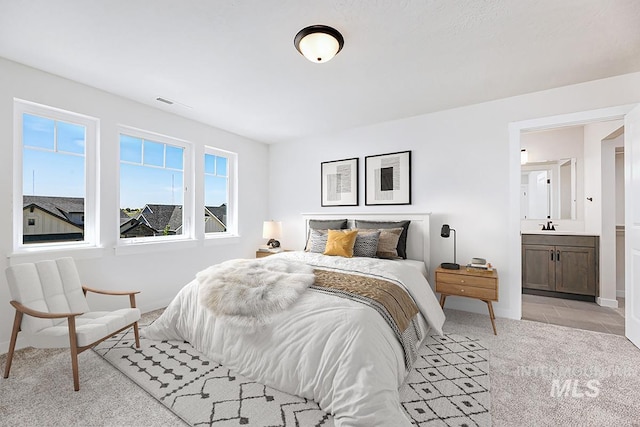 bedroom with light carpet, baseboards, connected bathroom, and a sink