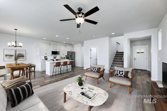 living room with wood finished floors, ceiling fan, stairway, a chandelier, and a textured ceiling
