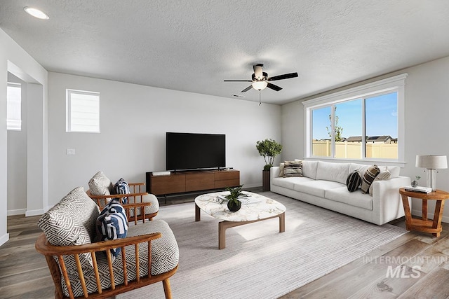 living room with wood finished floors, healthy amount of natural light, a ceiling fan, baseboards, and a textured ceiling