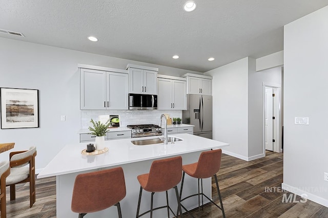 kitchen featuring appliances with stainless steel finishes, a sink, a breakfast bar, dark wood finished floors, and recessed lighting