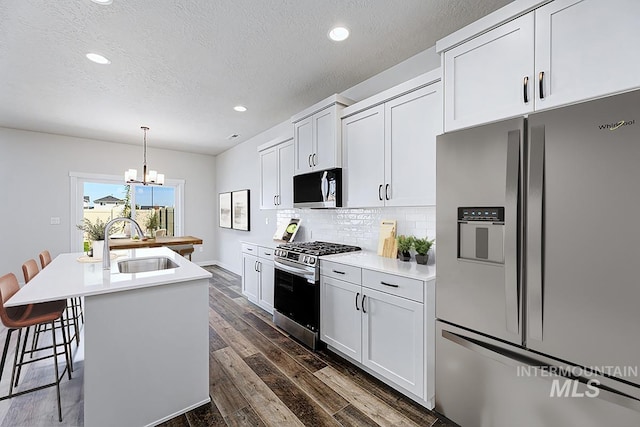 kitchen with stainless steel appliances, a sink, a kitchen island with sink, a chandelier, and light countertops