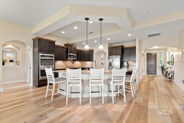 14942 Midway Rd, Nampa, ID 83651 - kitchen with appliances with stainless steel finishes, arched walkways, light wood-style flooring, dark brown cabinetry, and recessed lighting
