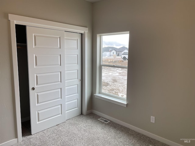 unfurnished bedroom with carpet flooring, multiple windows, visible vents, and a closet