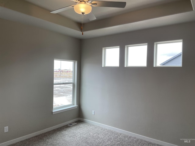 carpeted spare room featuring visible vents, baseboards, a raised ceiling, and ceiling fan