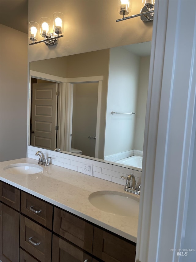 bathroom featuring a sink, decorative backsplash, toilet, and a bath