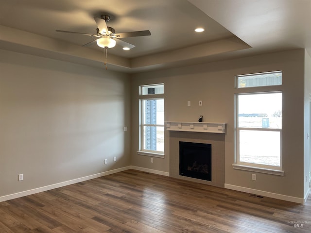 unfurnished living room with a tray ceiling, baseboards, dark wood-type flooring, and visible vents