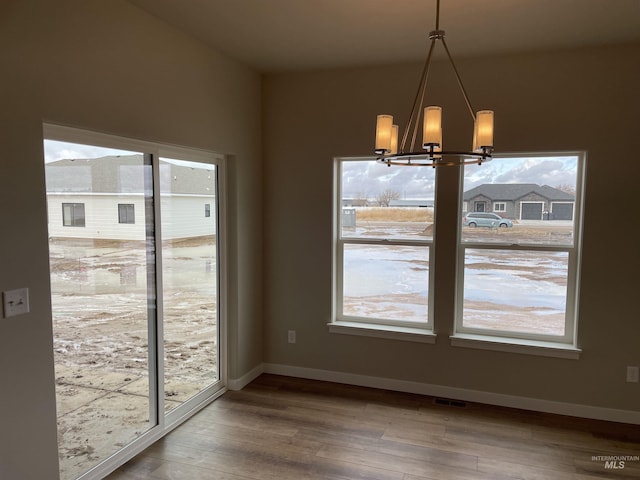 unfurnished dining area featuring wood finished floors, visible vents, a chandelier, and baseboards