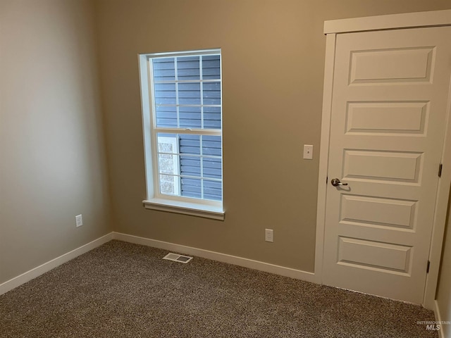 spare room with visible vents, baseboards, and dark colored carpet