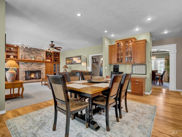 1546 N Dragonfly Ct, Eagle, ID 83616 - dining area with light wood-style floors, a ceiling fan, a stone fireplace, baseboards, and a textured ceiling