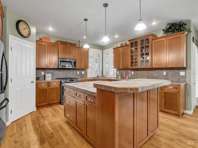 1546 N Dragonfly Ct, Eagle, ID 83616 - kitchen featuring light wood-style floors, stainless steel appliances, a kitchen island, brown cabinetry, and backsplash
