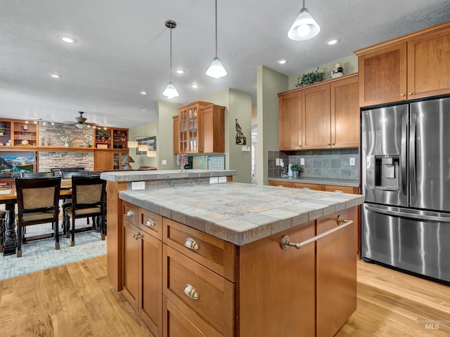 1546 N Dragonfly Ct, Eagle, ID 83616 - kitchen featuring brown cabinets, decorative backsplash, a kitchen island, light wood finished floors, and stainless steel fridge with ice dispenser