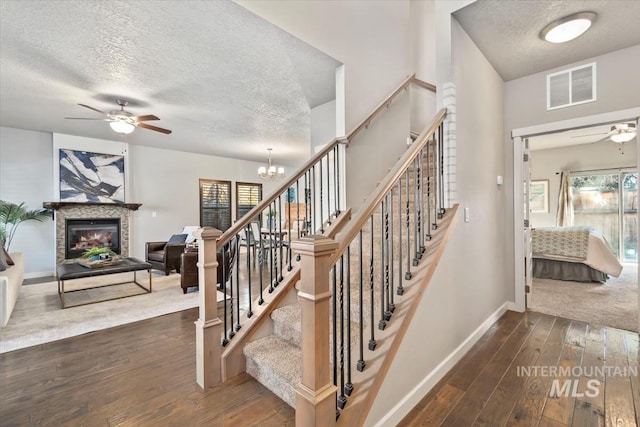 staircase with a textured ceiling, ceiling fan with notable chandelier, hardwood / wood-style flooring, and a tiled fireplace