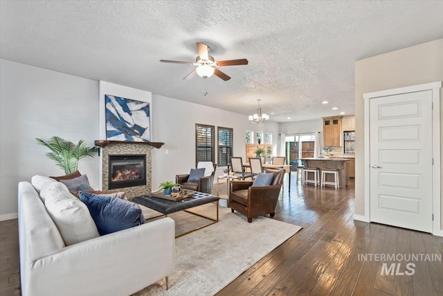 living room with ceiling fan with notable chandelier, dark wood-type flooring, and a textured ceiling