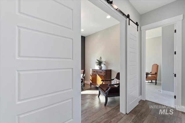 hallway featuring a barn door, baseboards, dark wood finished floors, and recessed lighting