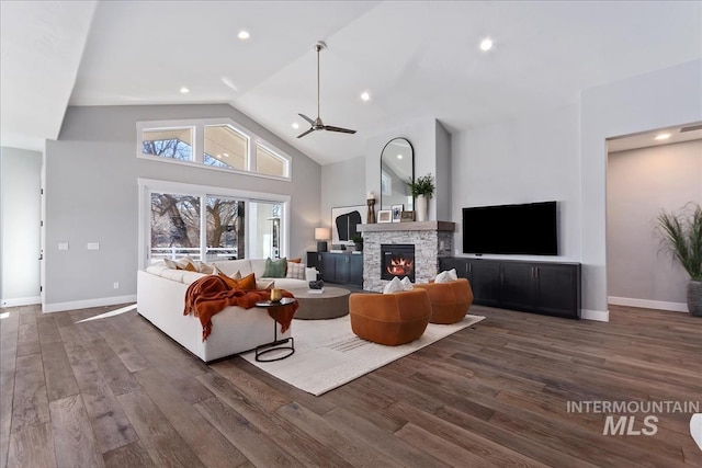 living room featuring high vaulted ceiling, a stone fireplace, baseboards, and wood finished floors