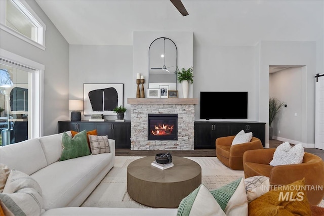 living area featuring a barn door, a fireplace, baseboards, and wood finished floors