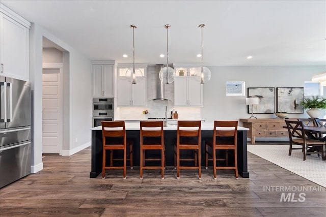 kitchen featuring a kitchen island with sink, stainless steel appliances, dark wood-style flooring, wall chimney exhaust hood, and glass insert cabinets