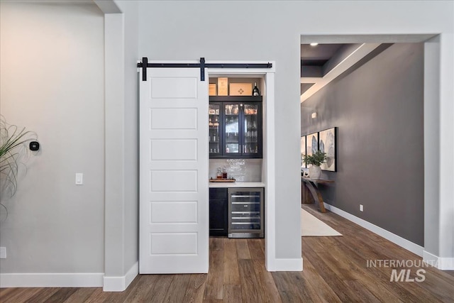 bar featuring wine cooler, dark wood finished floors, backsplash, a bar, and baseboards
