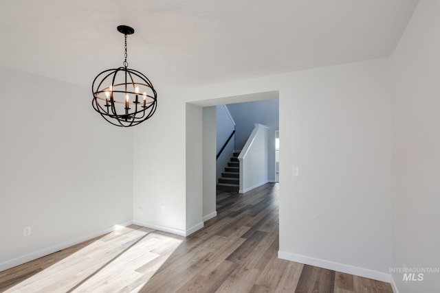 unfurnished room featuring stairs, light wood-style flooring, baseboards, and a chandelier