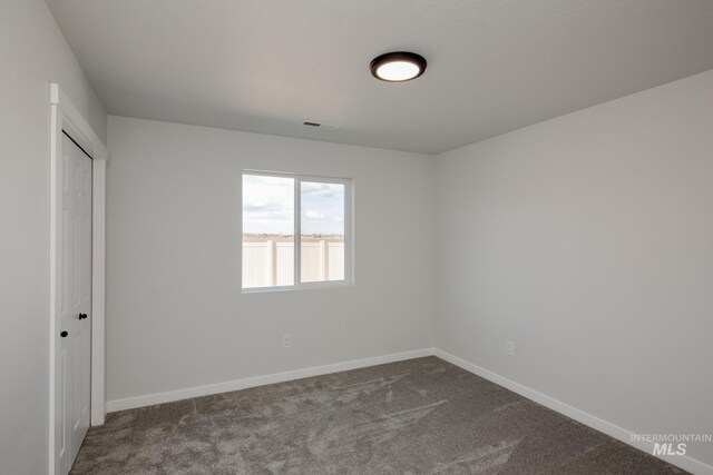 empty room featuring dark colored carpet and baseboards