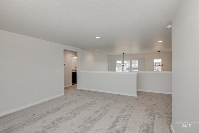 spare room with a notable chandelier, a textured ceiling, recessed lighting, carpet floors, and baseboards