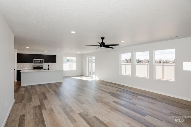 unfurnished living room featuring a textured ceiling, wood finished floors, recessed lighting, baseboards, and ceiling fan