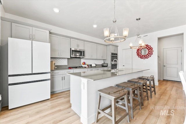11211 Sopris Loop, Caldwell, ID 83605 - kitchen with stainless steel appliances, a chandelier, light wood-type flooring, an island with sink, and tasteful backsplash