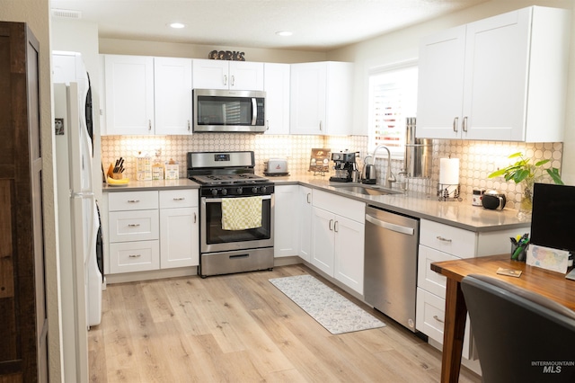 kitchen featuring sink, light hardwood / wood-style flooring, appliances with stainless steel finishes, white cabinetry, and decorative backsplash