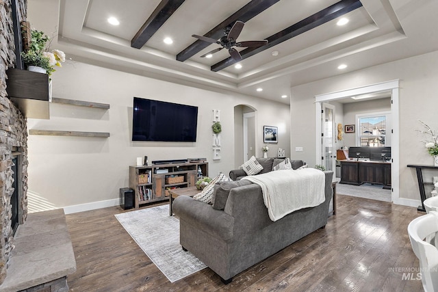 living room featuring baseboards, a tray ceiling, arched walkways, and dark wood-type flooring