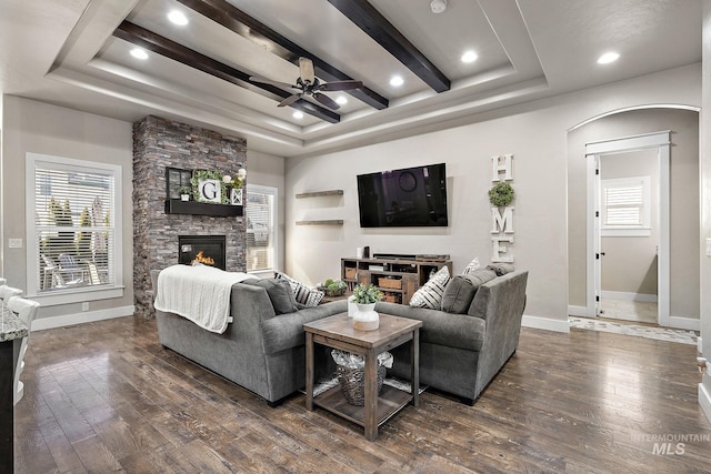 living room featuring a raised ceiling, dark wood finished floors, a stone fireplace, and baseboards