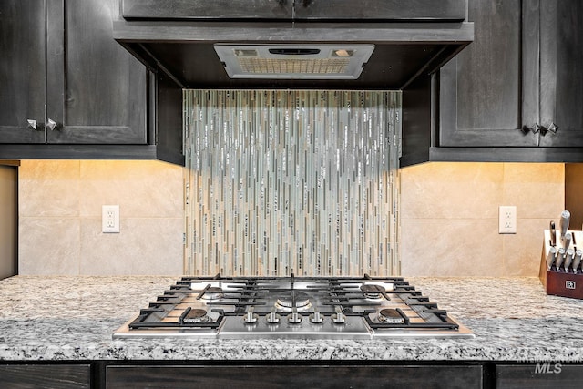 kitchen featuring stainless steel gas cooktop, light stone counters, exhaust hood, and decorative backsplash