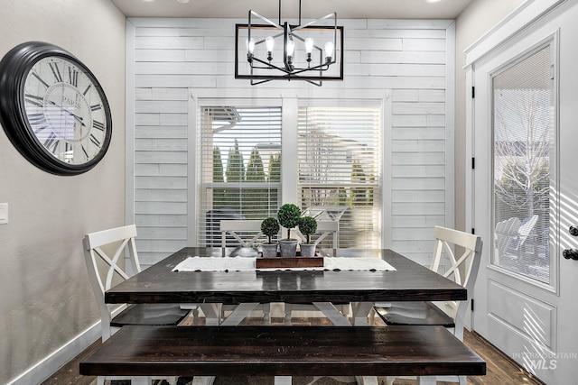 dining room with dark wood-type flooring, wood walls, baseboards, and an inviting chandelier