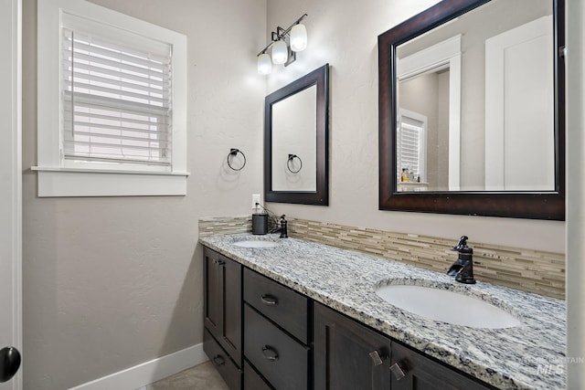 bathroom featuring a textured wall, a sink, baseboards, and double vanity