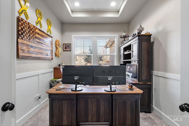 office space with light carpet, wainscoting, a raised ceiling, and a decorative wall