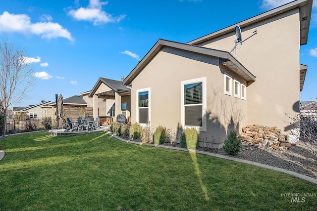 rear view of property featuring a yard, a patio area, fence, and stucco siding