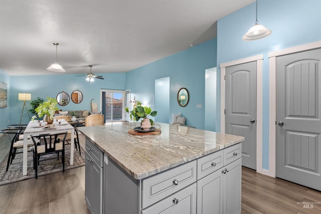 kitchen with a kitchen island, hardwood / wood-style floors, pendant lighting, and light stone countertops