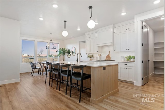 kitchen with a breakfast bar area, light countertops, custom range hood, light wood-style floors, and a kitchen island with sink