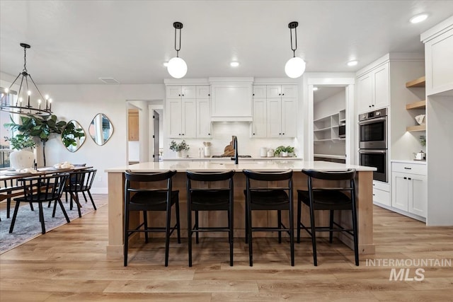 kitchen featuring light countertops, light wood-style flooring, stainless steel double oven, and white cabinetry