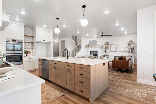 kitchen featuring open shelves, light countertops, appliances with stainless steel finishes, a glass covered fireplace, and a sink