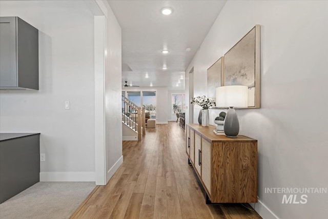 hall featuring light wood-type flooring, stairway, and baseboards