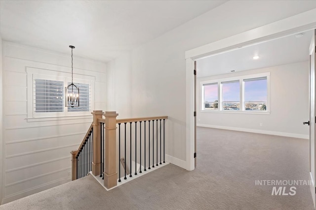 hallway featuring carpet, baseboards, a notable chandelier, and an upstairs landing