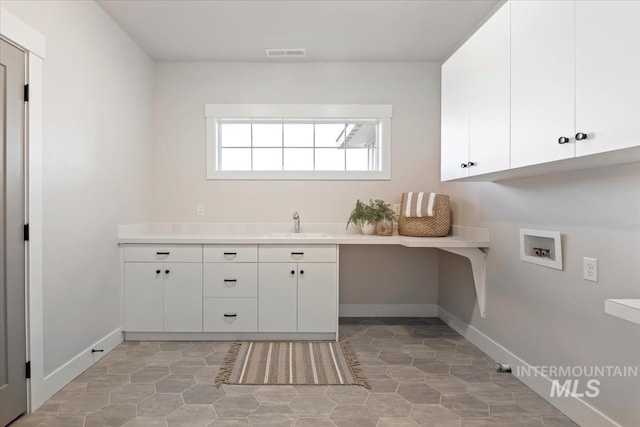 clothes washing area featuring washer hookup, cabinet space, visible vents, a sink, and baseboards