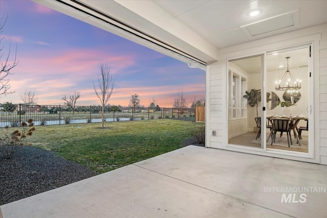 patio terrace at dusk with a water view, a fenced backyard, and a lawn