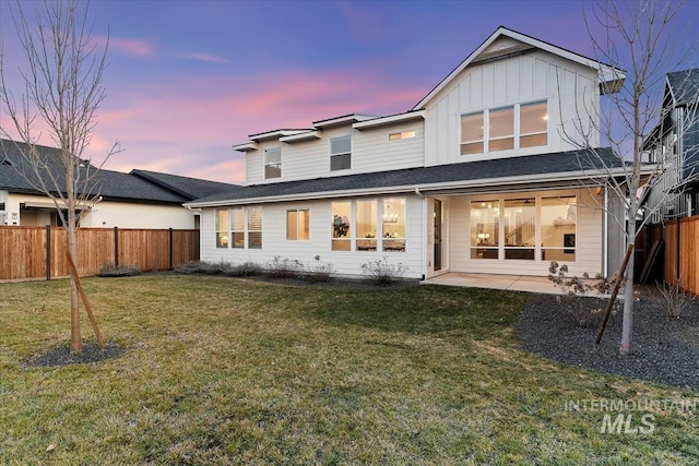 back of property at dusk with board and batten siding, a fenced backyard, a lawn, and a patio